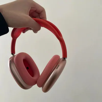 Pink over-ear headphones held up by the headband against a plain wall