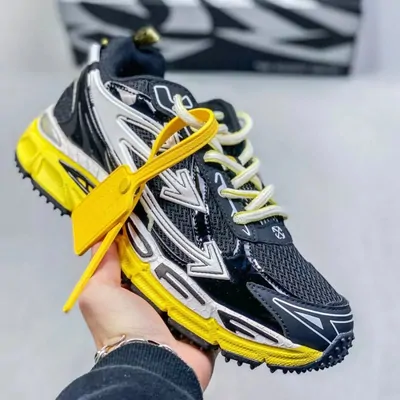 Black and yellow trail sneaker held in one hand