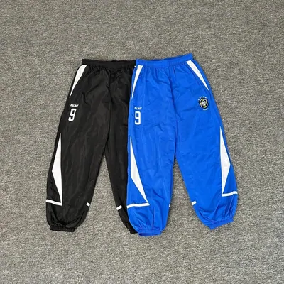 Two pairs of track pants, one black and one blue, side by side on grey carpet