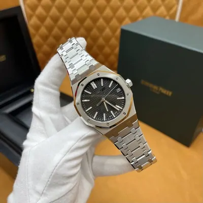 Steel-coloured bracelet watch with a dark dial held in a white glove